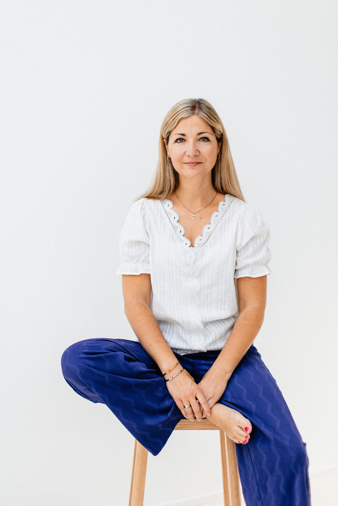 Sabrina Milewski sitzt lächelnd im Jeans-Overall auf einem hellen Sofa